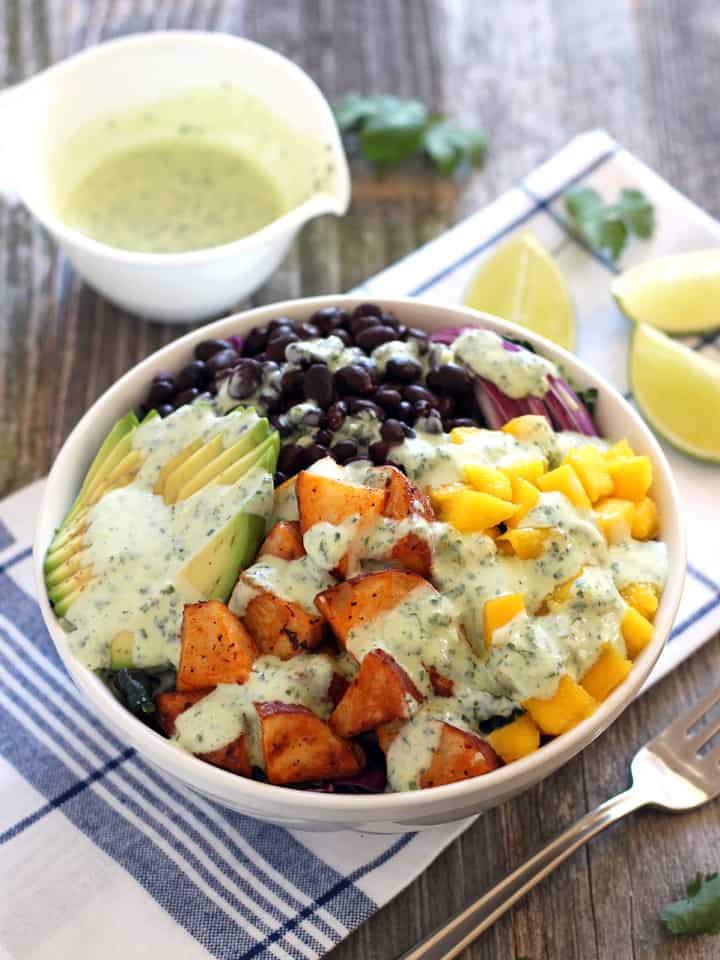 A white bowl with salad next to a cup of dressing.