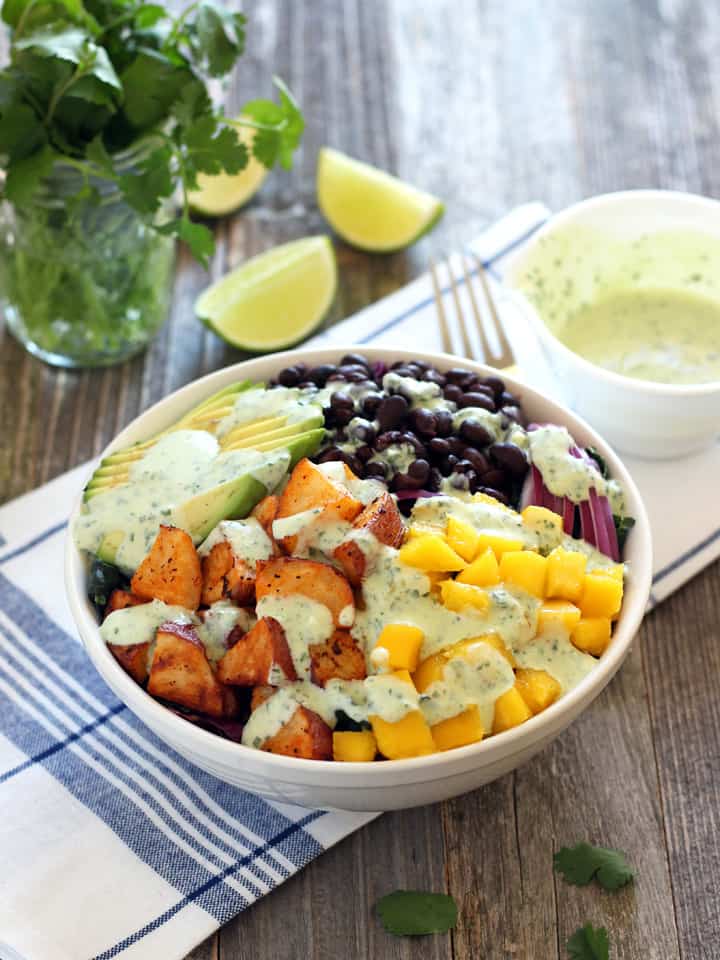 A wooden table with a big bowl of salad and cilantro in a glass jar.