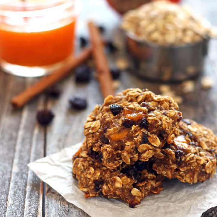 Pile of oatmeal cookies on a table with oats and cinnamon sticks.