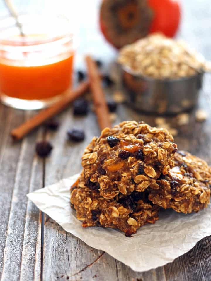 Pile of oatmeal cookies on a table with oats and cinnamon sticks.