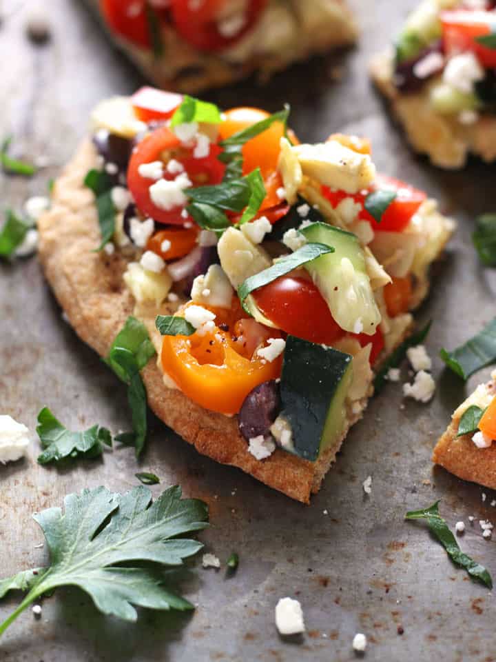 Close up of a slice of flatbread topped with hummus and fresh veggies.