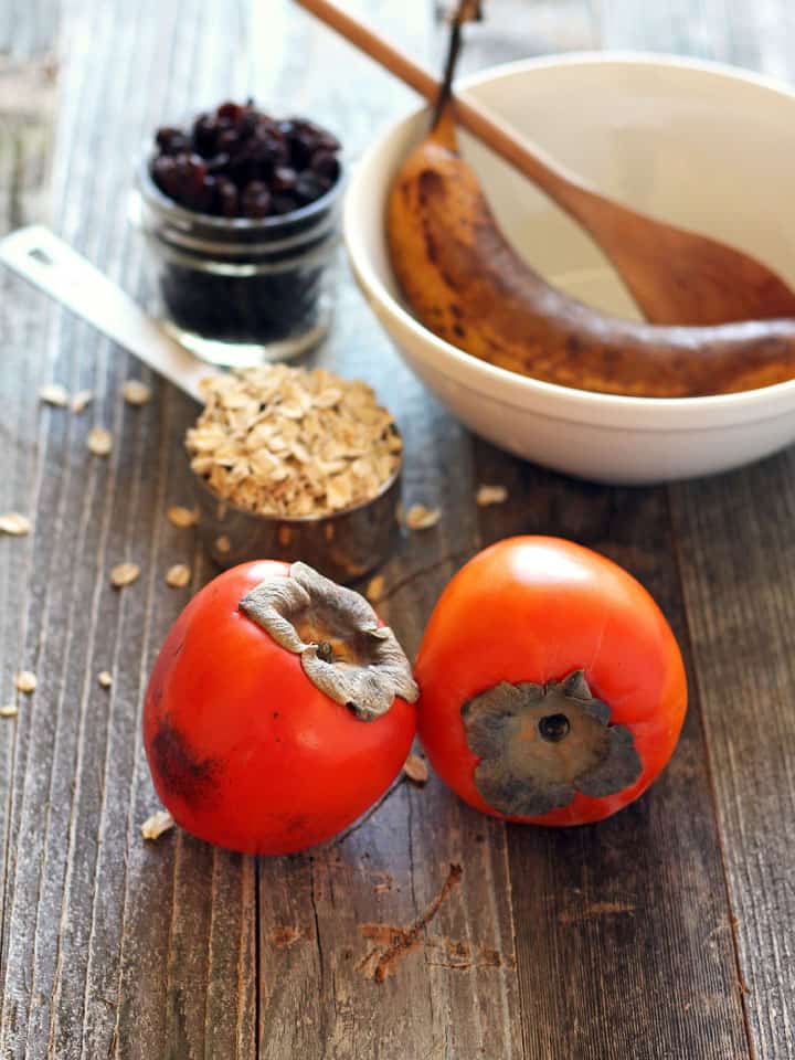 Hachiya persimmons, oats, raisins, and a banana on a wooden table.