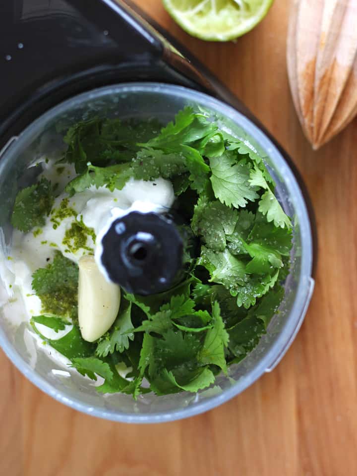 Overhead photo of a mini food processor filled with cilantro and garlic. 