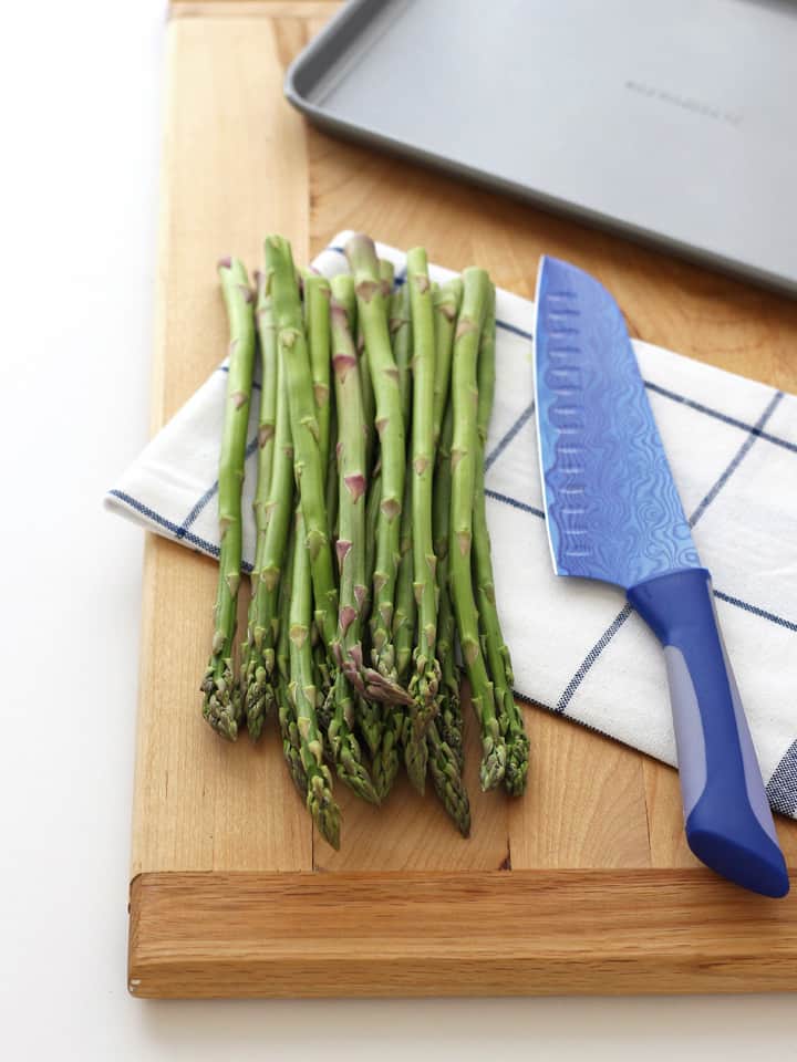 Bunch of fresh asparagus on a cutting board with a knife.