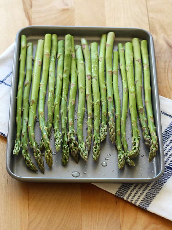 Asparagus spears on a toaster oven baking sheet drizzled with oil.