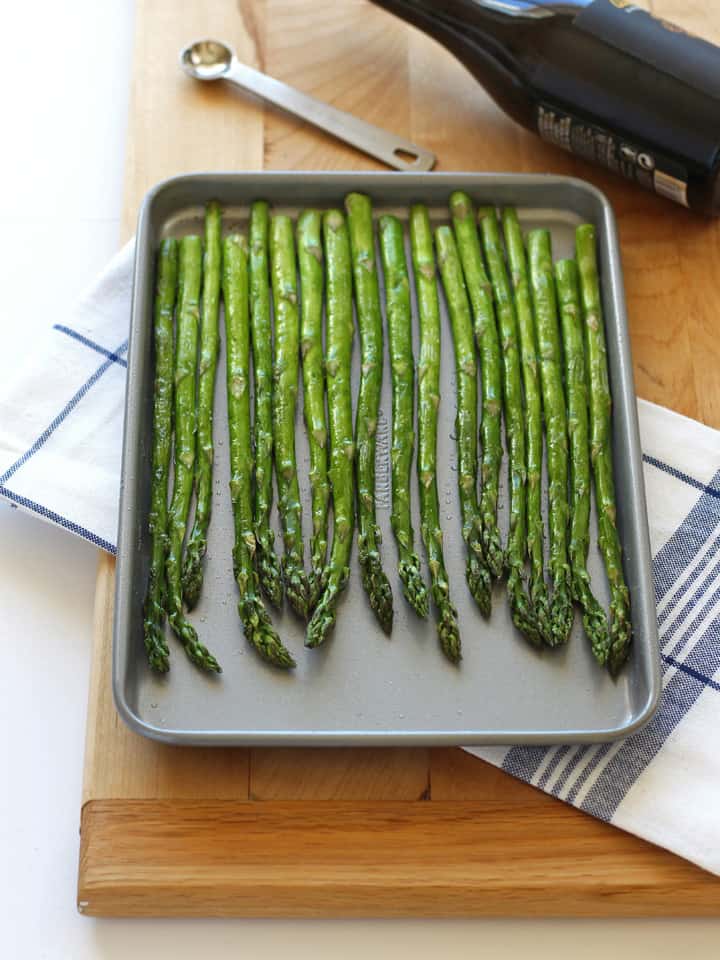 Roasted asparagus spears next to a bottle of balsamic vinegar.