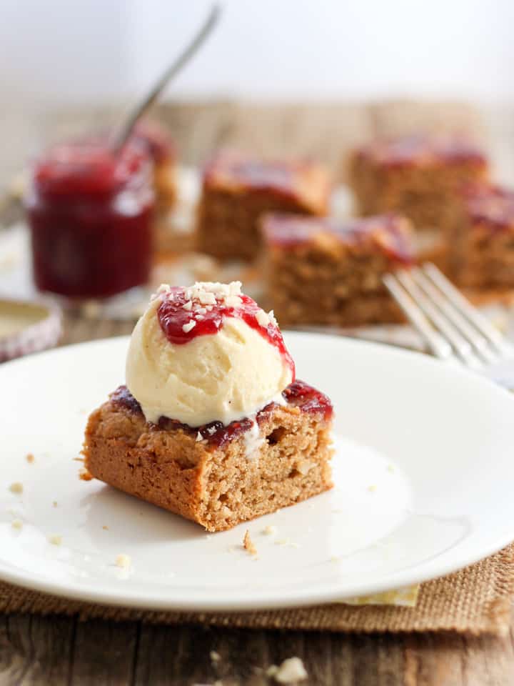 White plate with a peanut butter bar topped with vanilla ice cream and berry preserves.