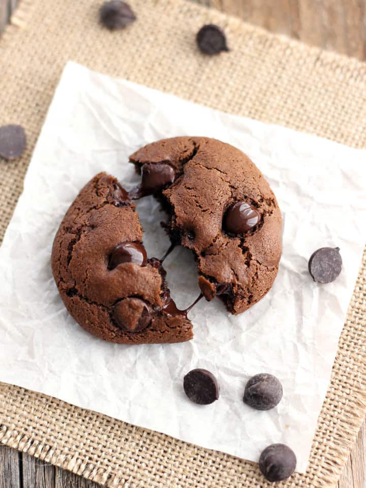 Cookie split in half on a piece of parchment surrounded by chocolate chips.