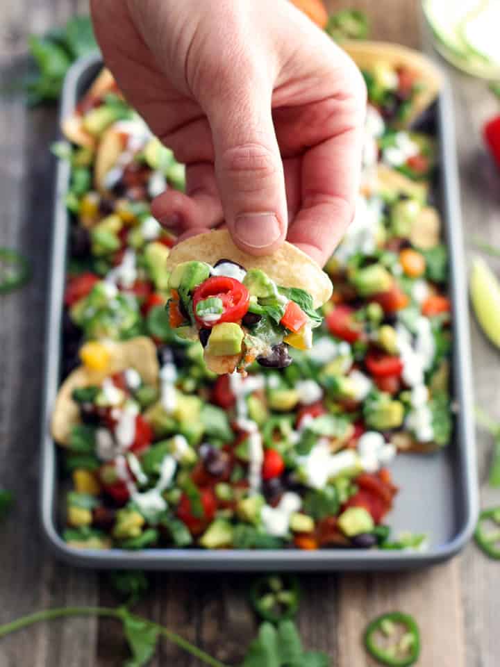 Hand scooping up a chip from a pan of veggie nachos.