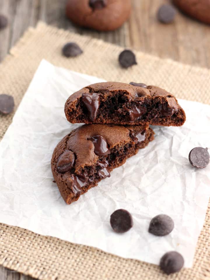 Two halves of a gooey cookie on a piece of parchment with chocolate chips.