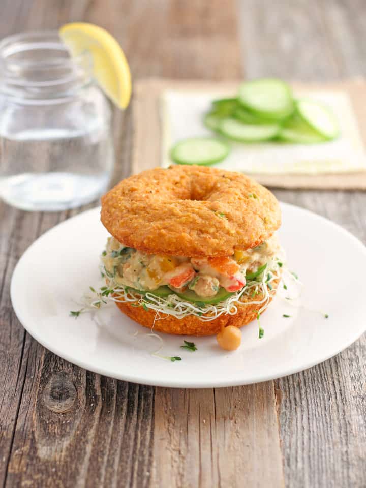 A wooden table with a glass of water, cucumber slices, and veggie-stuffed sandwich.