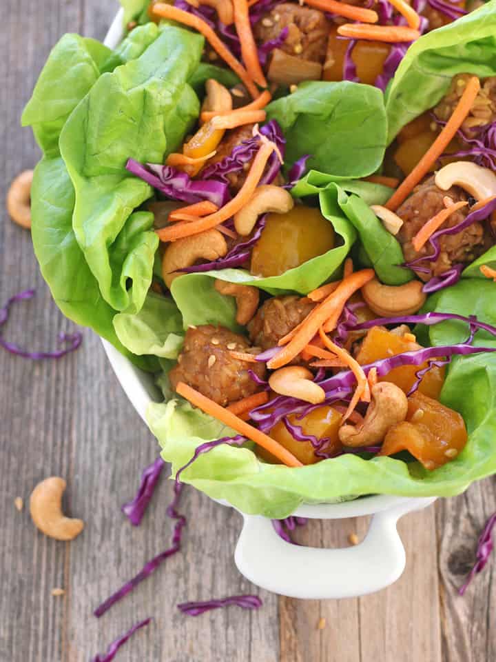 Serving dish full of lettuce wraps topped with carrots, purple cabbage, and cashews.