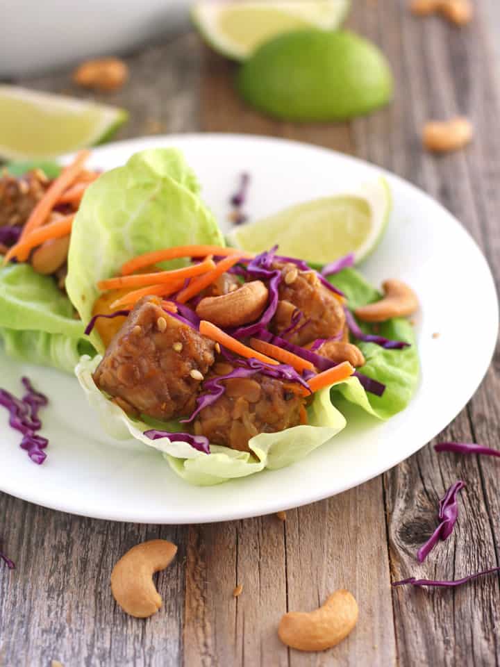 Tempeh lettuce wraps on a white plate with lime wedges and cashews.