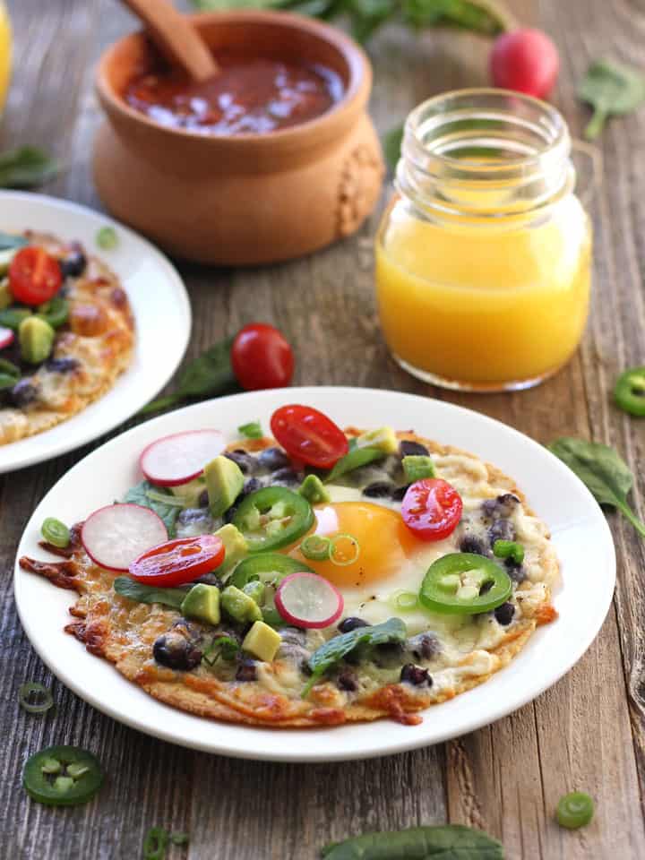 White plate with a baked tostada on a wooden table with glass of orange juice.