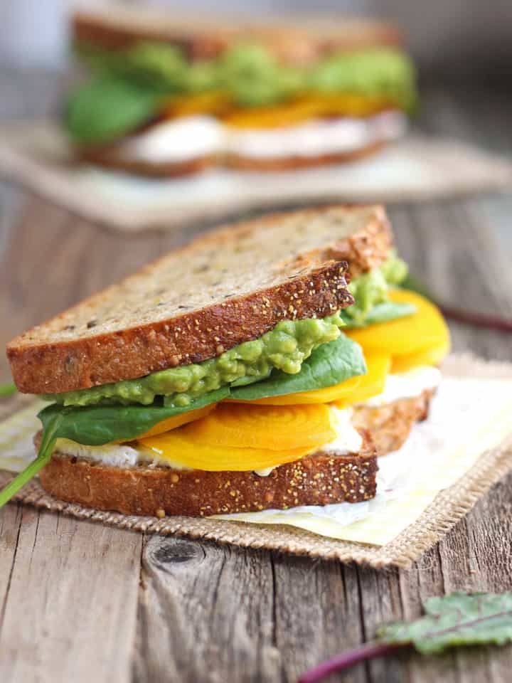 Layers of avocado, beet, and ricotta sandwich between two slices of toasted bread.