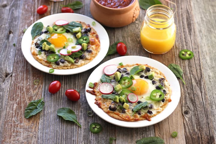 Two white plates with egg tostadas with a glass of orange juice and pot of salsa on a table.