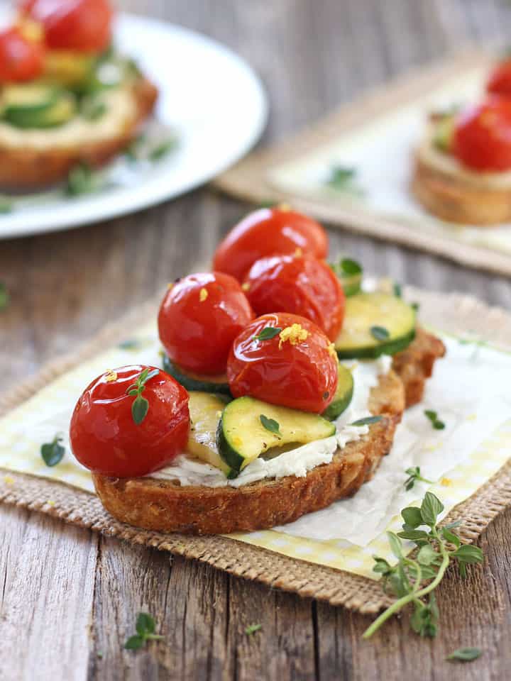 Juicy tomatoes on a goat cheese topped crostini on a wooden table.