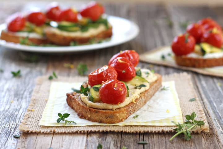 3 crostini on a plate and parchment squares on a wooden table.