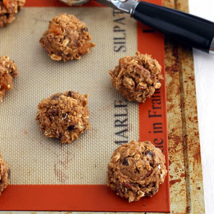 Raw cookie dough balls on a toaster sheet pan lined with a baking mat.