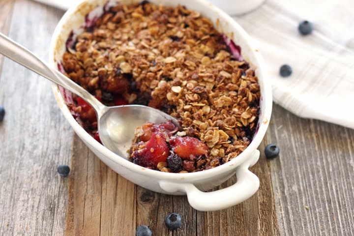 A baking dish of mango blueberry crisp on a wooden table.