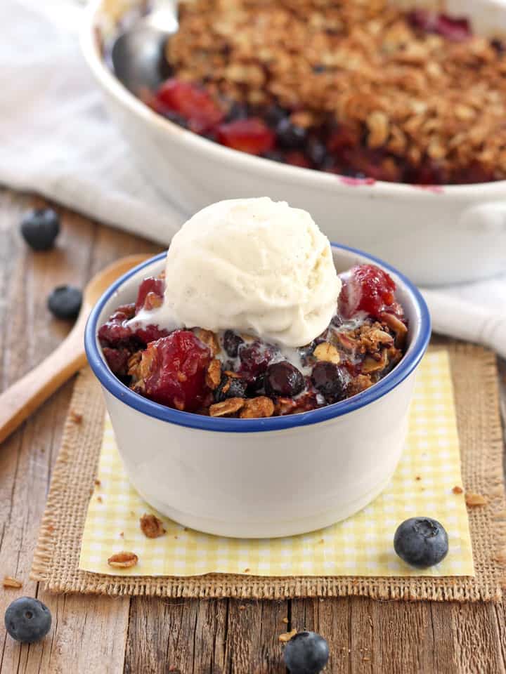 Small bowl of fruit crisp topped with vanilla ice cream.