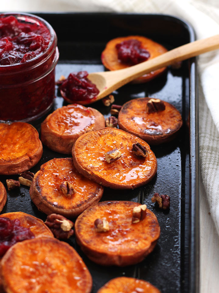 Roasted sweet potato rounds topped with pecans with a small jar of cranberry sauce.