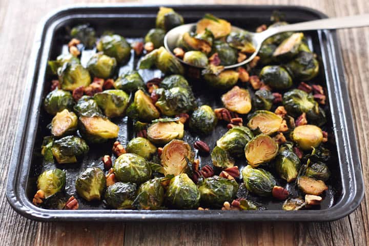 Cooked Brussels sprouts on a small sheet pan with a large metal spoon.