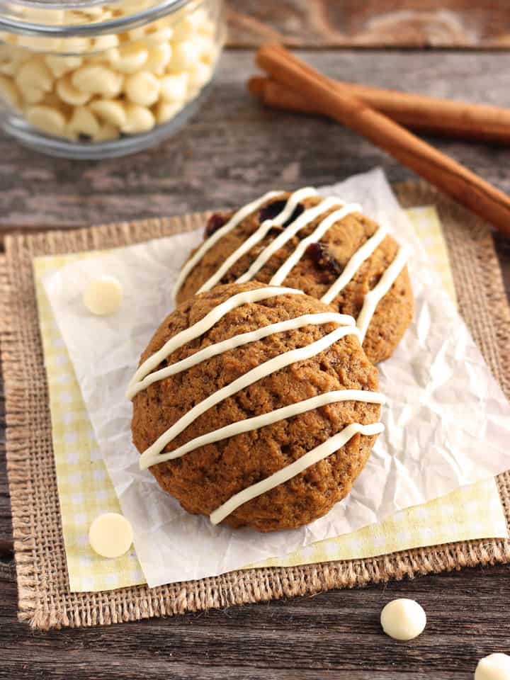 Two cookies drizzled with white chocolate on a piece of parchment paper.