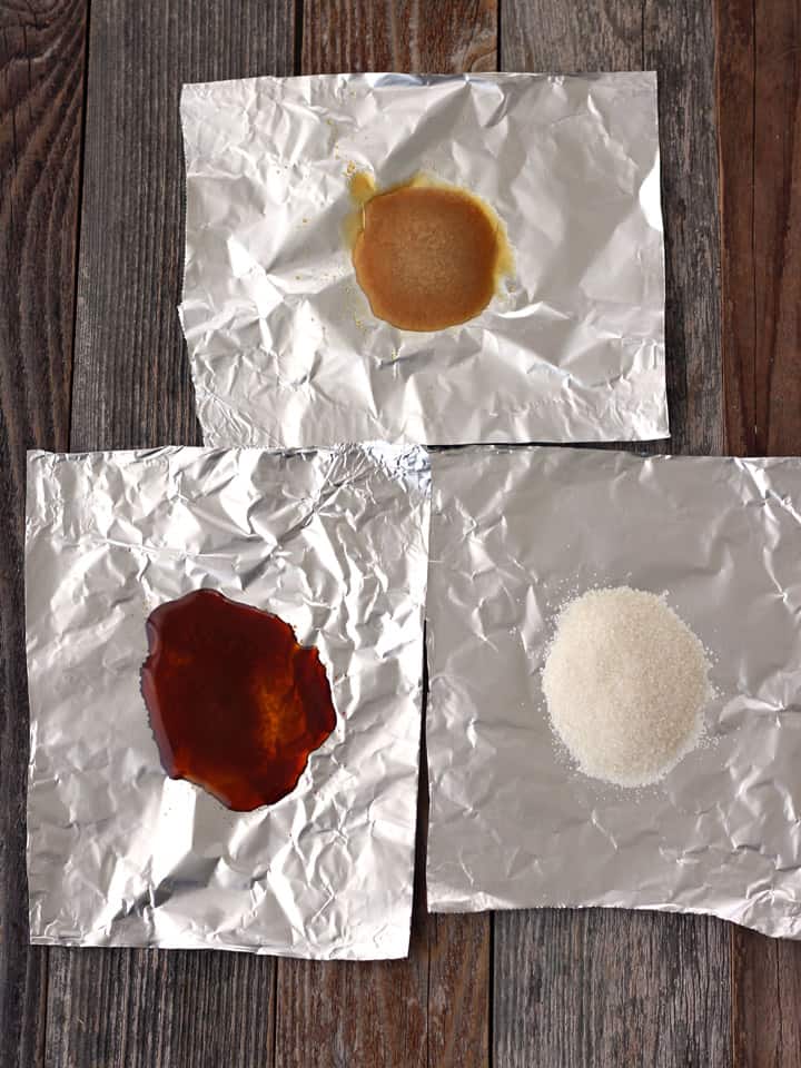 Overhead view of burnt, browned, and white sugar on pieces of foil.