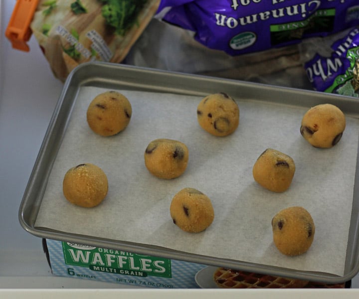 Cookie dough balls on a baking sheet inside a freezer.