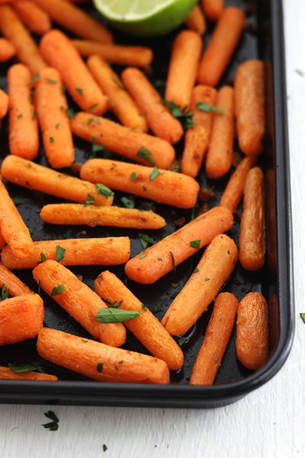 A dark roasting pan with cooked baby carrots.