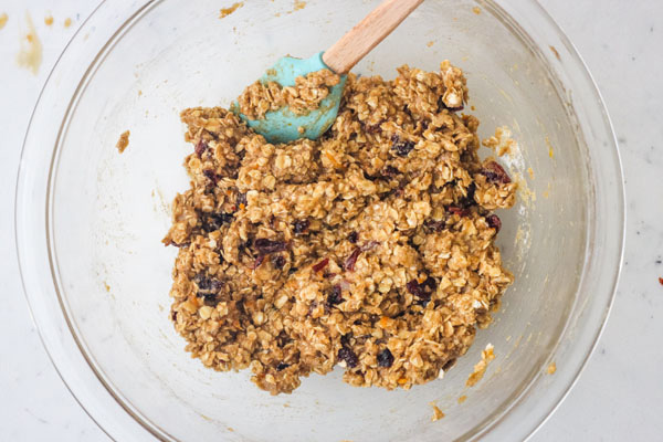 Oatmeal cookie dough in a glass bowl with a blue rubber spatula.