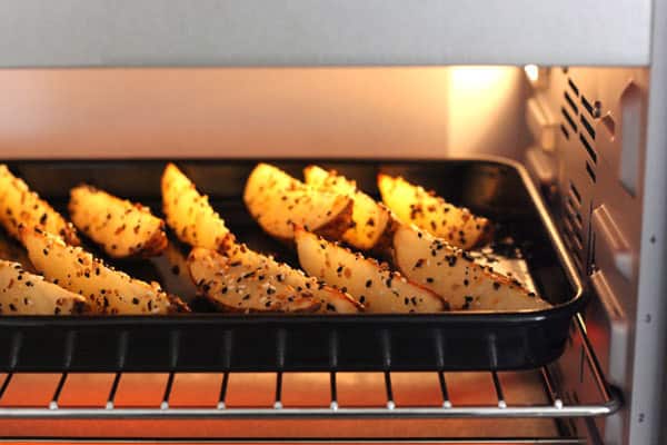 Potato wedges on a baking sheet baking inside a toaster oven.