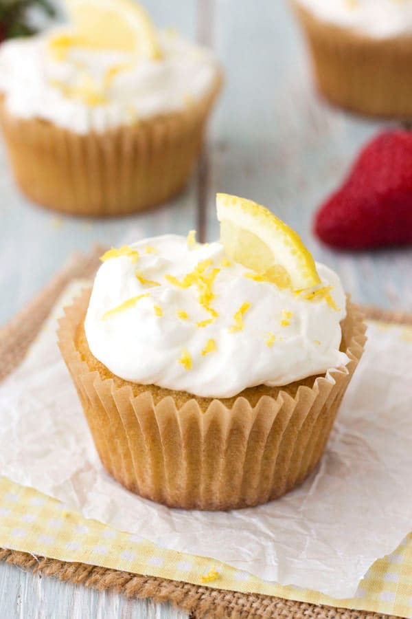 Cupcake topped with whipped cream and lemon zest on a piece of parchment.