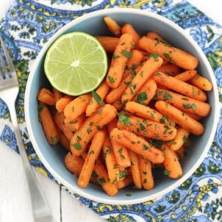 Overhead view of roasted baby carrots and half a lime.