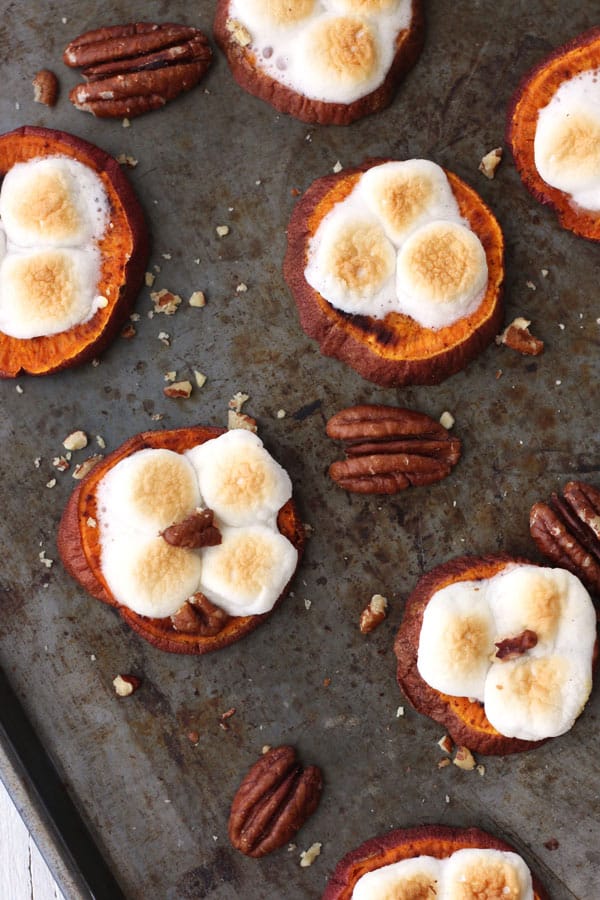 Broiled mini marshmallows and pecans on a pan of baked sweet potato rounds.