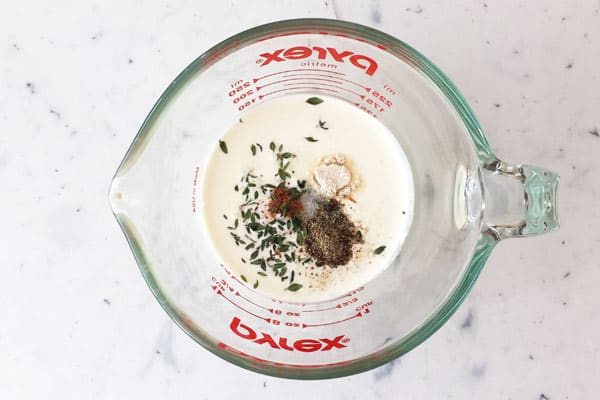 Cream in a measuring glass with seasonings and fresh thyme