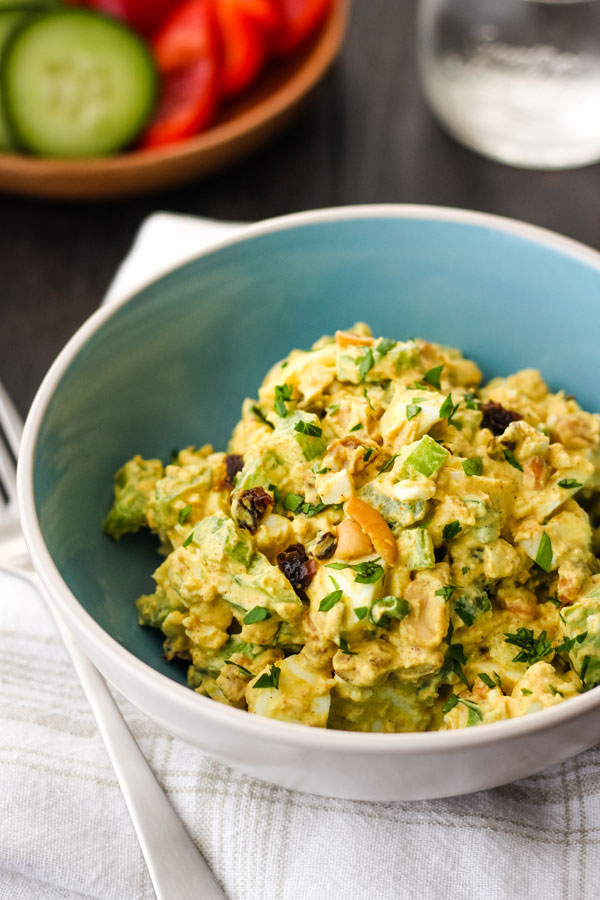 Egg Salad in a blue bowl with a wooden bowl of fresh veggies.