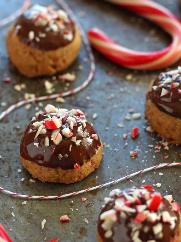 Chocolate-dipped cookies on a baking sheet with a candy cane and crushed peppermint candies.