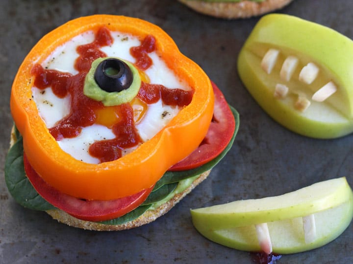 Eggs baked in orange bell pepper slices next to apples with almond 'vampire' teeth.