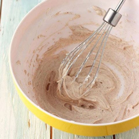 Cream cheese frosting whipped in a yellow bowl with a whisk.