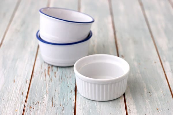 White ramekins stacked on a blue wooden table.