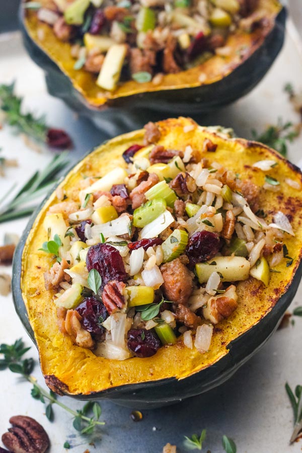 Stuffed roasted acorn squash half on a baking sheet with pecans and fresh herbs.