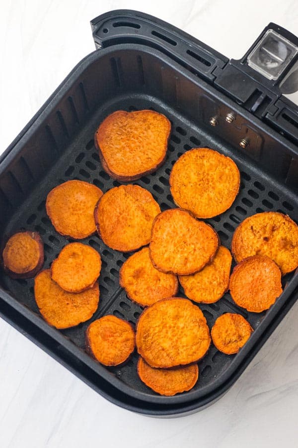 Cooked sweet potato slices in an air fryer basket.