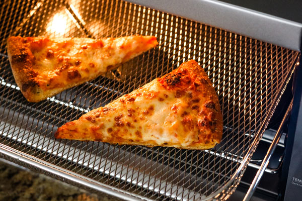 Cheese pizza slices in a metal basket inside a toaster oven.