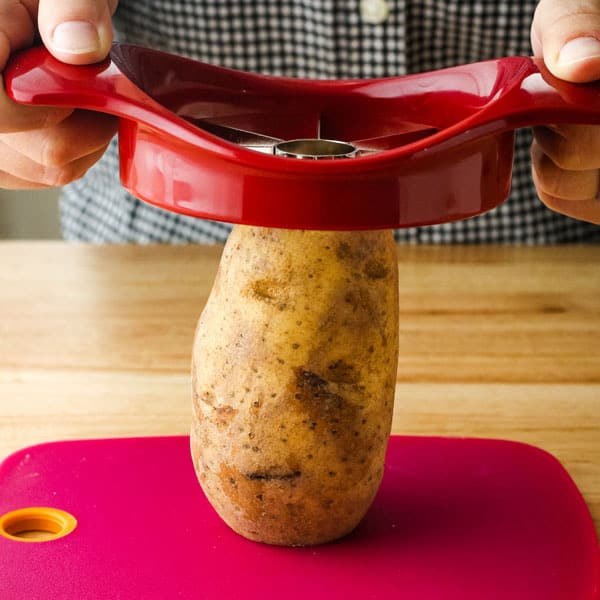 Hands holding an apple corer over a potato standing on a cutting board.