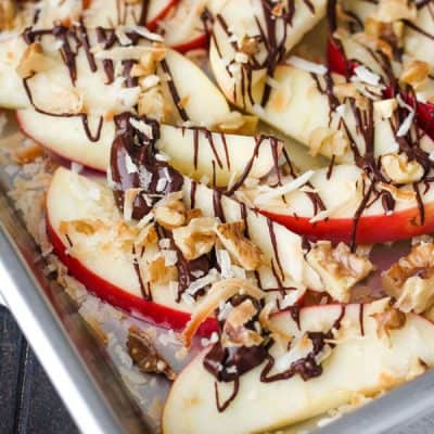 Apple nachos with drizzled chocolate and chopped nuts on a small baking pan.