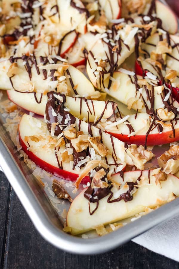 Apple slices with drizzled chocolate and chopped nuts on a small baking pan.