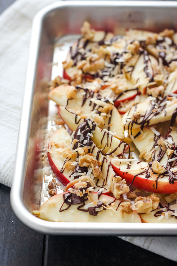 Apple slices topped with melted chocolate on a toaster oven sheet pan.