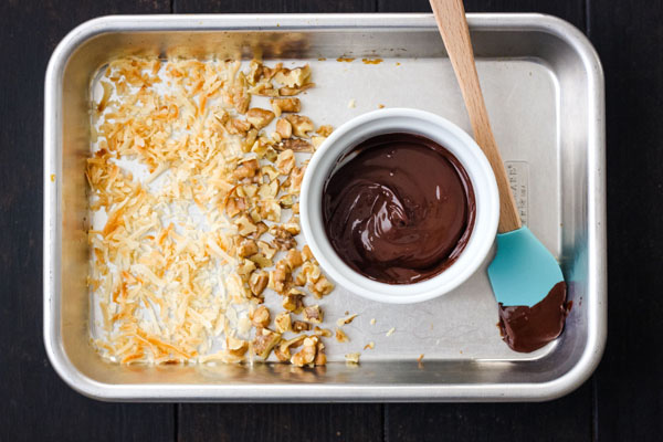 A 1/8th baking sheet with toasted coconut, nuts and a ramekin of melted chocolate.